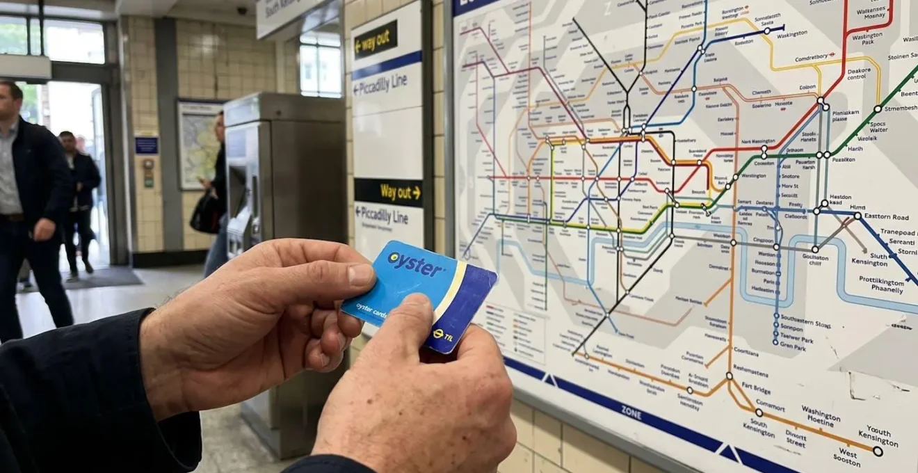 Gros plan sur des mains tenant une carte Oyster bleue avec un plan de métro londonien flouté en arrière-plan